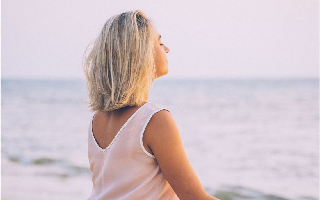 Femme assise face à la mer, visage tourné vers l'horizon