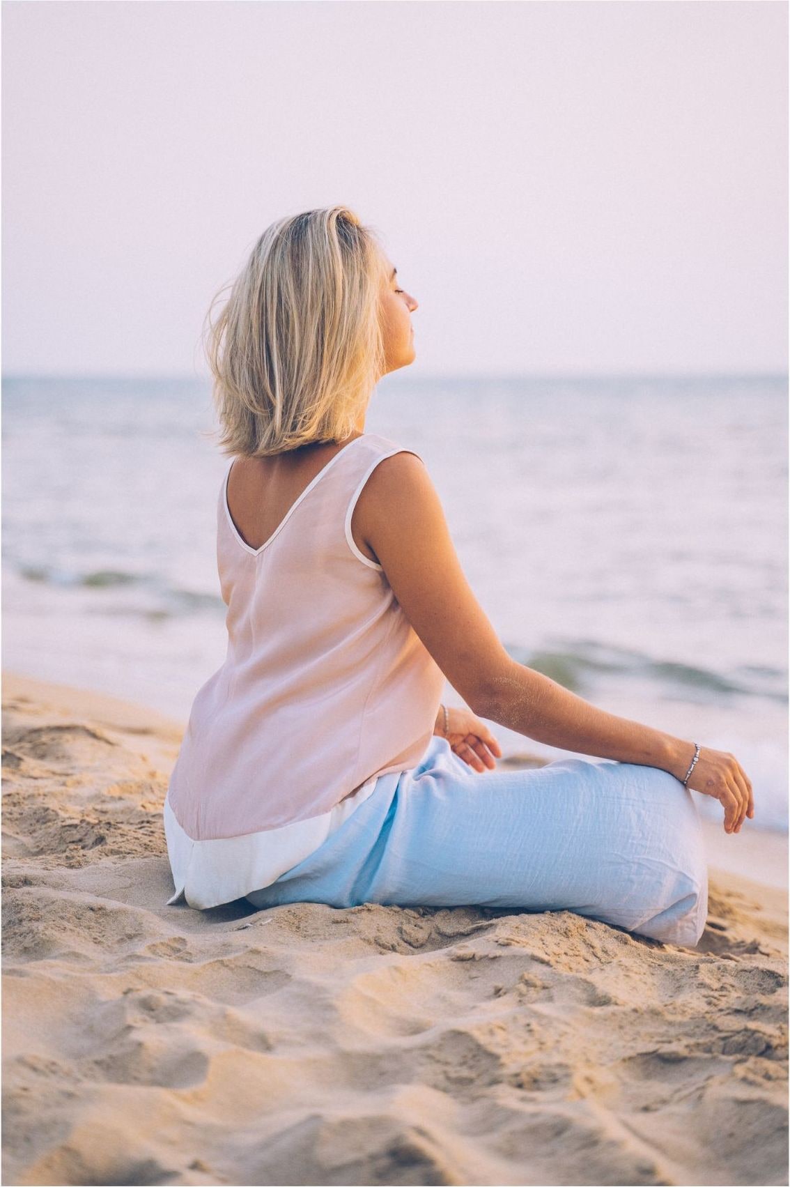 Femme assise en méditation face à la mer au coucher du soleil